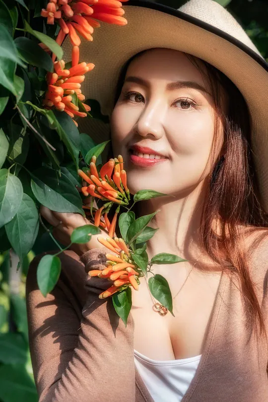 一位戴帽子的年轻女子在红色和橙色花朵的植物旁边为肖像摆姿势