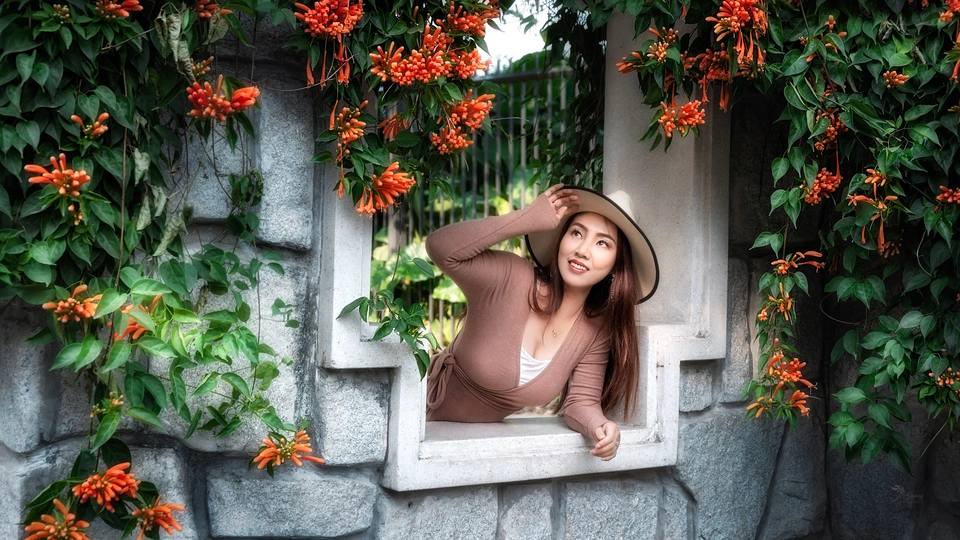 一位戴帽子的年轻女子正在窗前凝视着墙上红色的花朵。