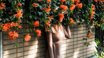 一位女性靠在墙上 头上戴着橙色花朵