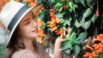 一位美丽的年轻女士戴着条纹帽子 正在看橙花。