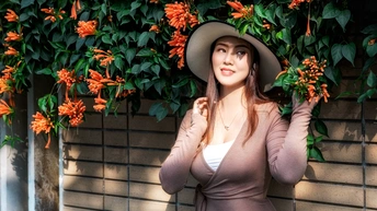 一位穿着棕色连衣裙和帽子 站在橙色花朵墙前的美丽年轻女子。