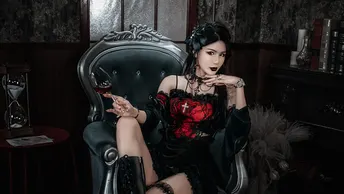 一个穿着黑色和红色连衣裙的女人坐在一个黑暗的房间里的一把椅子上 手里拿着一杯酒。