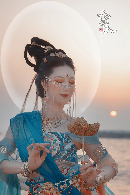 一位穿着蓝色传统服装的美女 背景中有一尊月亮形状的雕像。