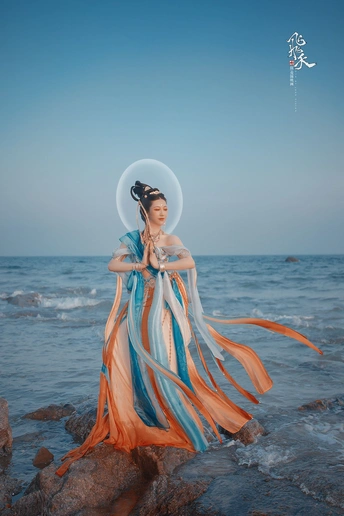 美丽的穿蓝色裙子的女人站在海滩上吹着水中的气泡