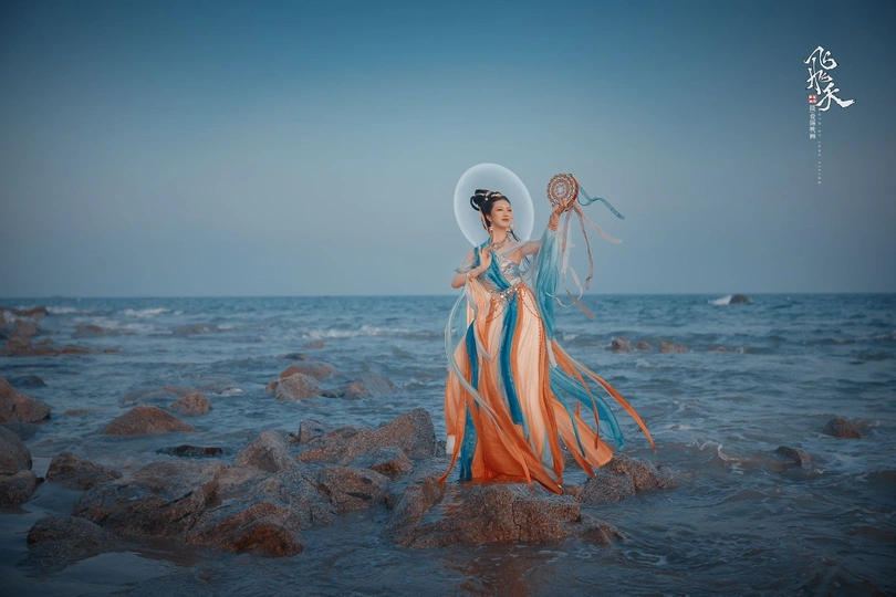 一位穿着连衣裙的美女站在海滩上的岩石上