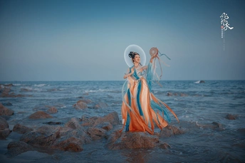 一位穿着连衣裙的美女站在海滩上的岩石上