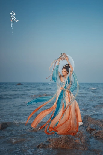 美丽的女子穿着蓝色裙子站在海滩附近的水边