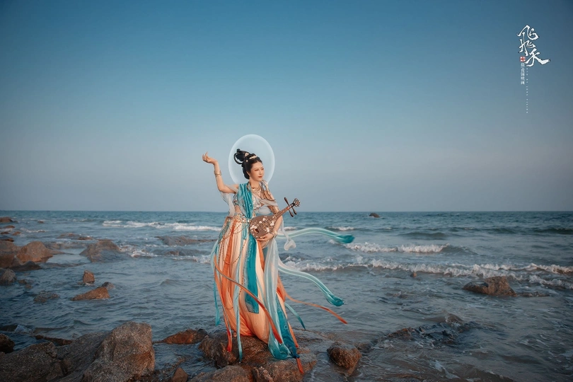 一位穿着连衣裙的女人站在岩石上 靠近海洋。