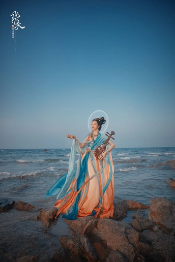 一位穿着蓝色连衣裙的美女站在海边的岩石上