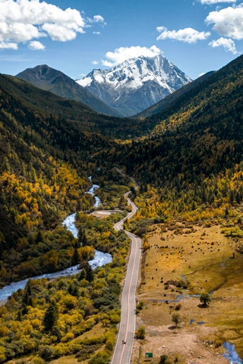 一条蜿蜒曲折的山间小路 穿过山谷 背景是河流和山脉。