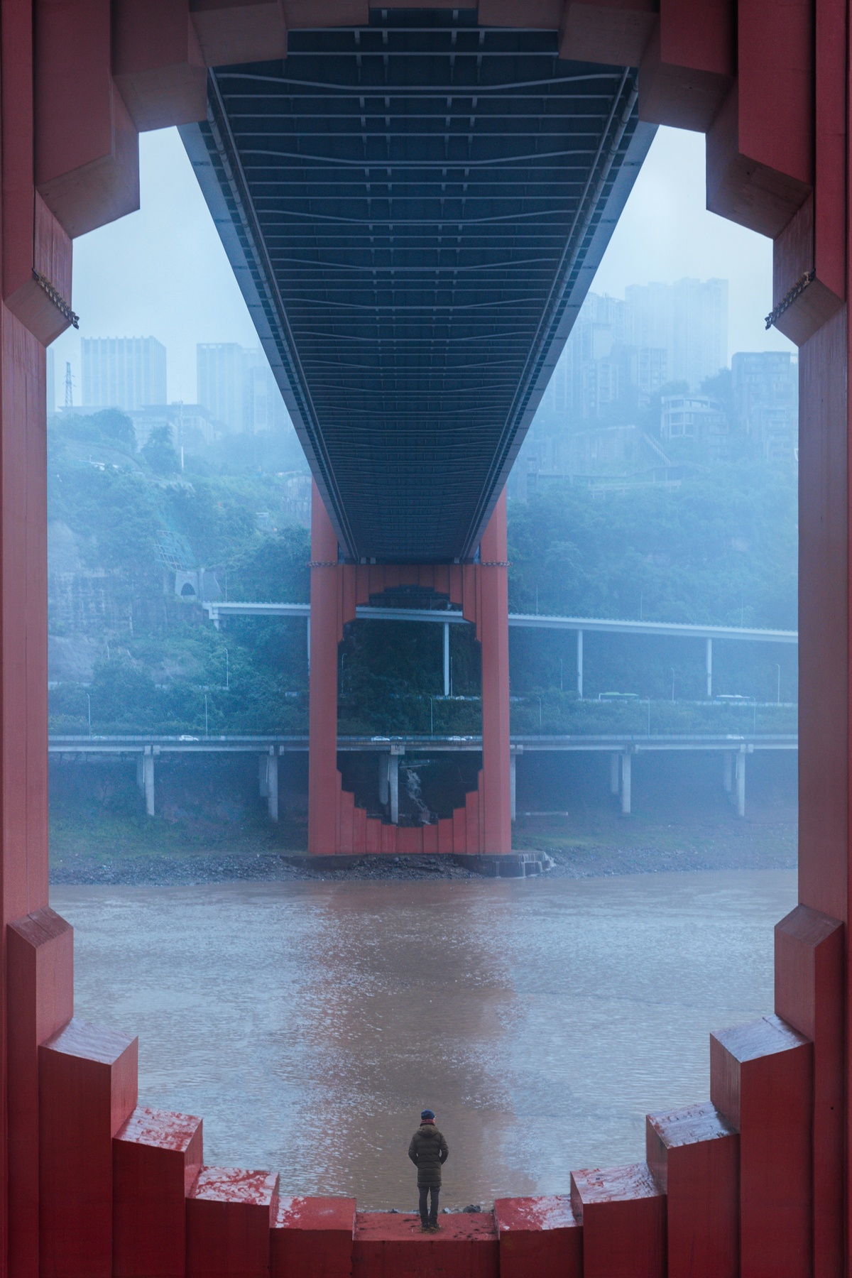 一个男人站在红桥下 雨中望着河对岸。