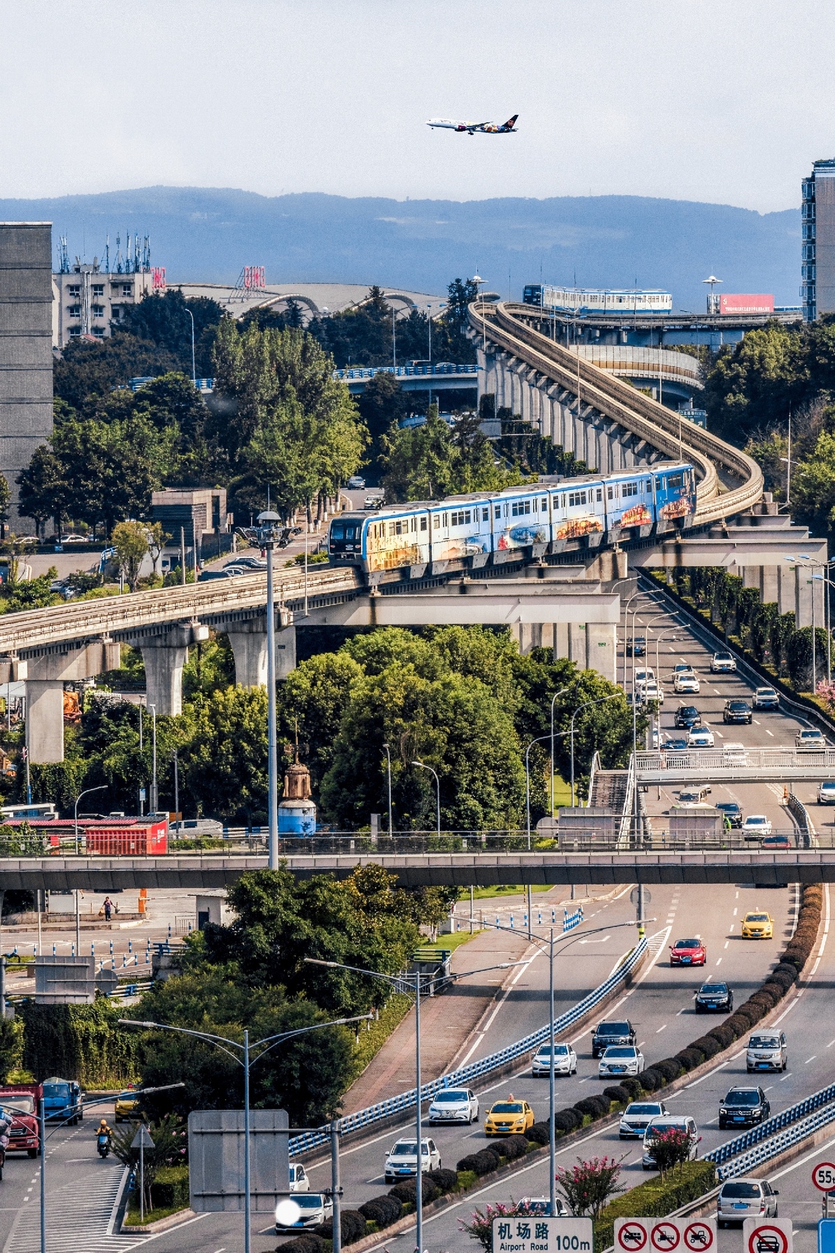 一架飞机飞越一个充满众多交通的城镇和一辆蓝色的火车在公路上行驶。