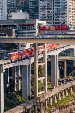 一列红色的火车穿越一座旁边有高楼大厦的桥。