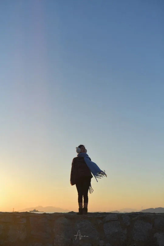 一个站在墙上的男人正在注视着一个站在岩石上观看日落的女人