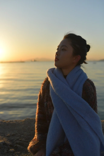 一个年轻女子裹着浴巾坐在海滩上 凝视着海洋上美丽的落日。