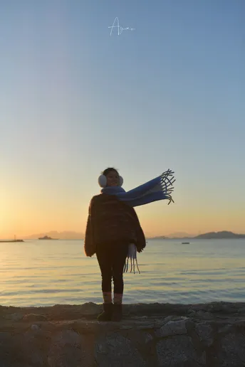 一位站在岩石上 凝视着夕阳下的海洋 太阳从水面上升起的女性的画面。