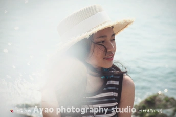 一位年轻女子戴着白色帽子 穿着条纹上衣 正在岩石上坐着 戴着草编帽子 靠近海。