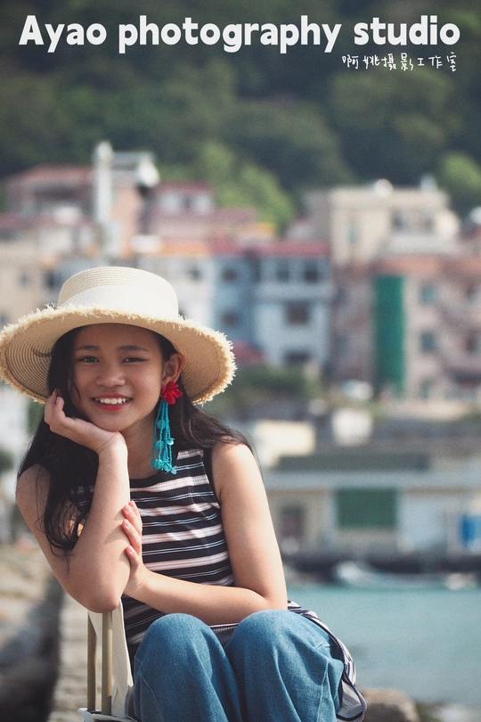 一个戴草帽的年轻女子坐在靠水边的椅子上