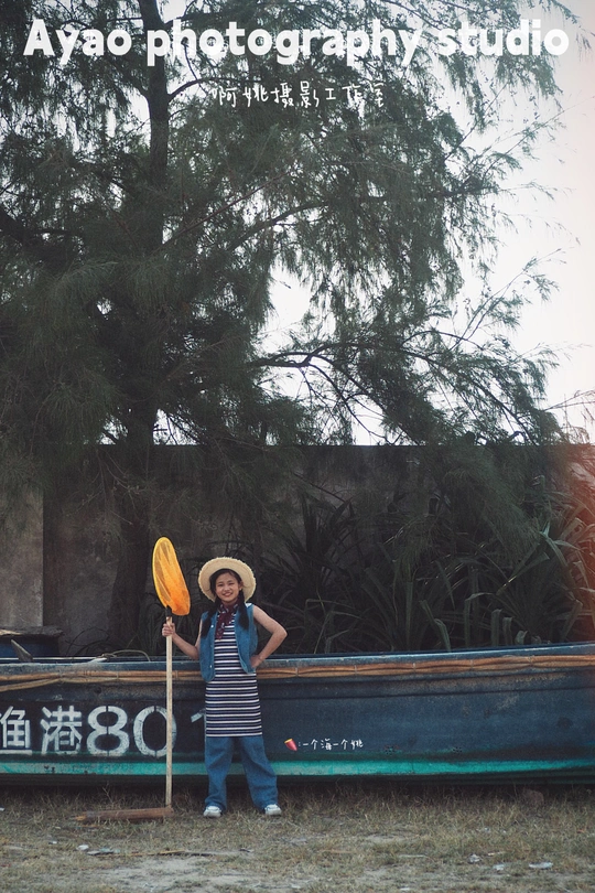 一个戴帽子的男孩拿着桨站在一艘小船旁边