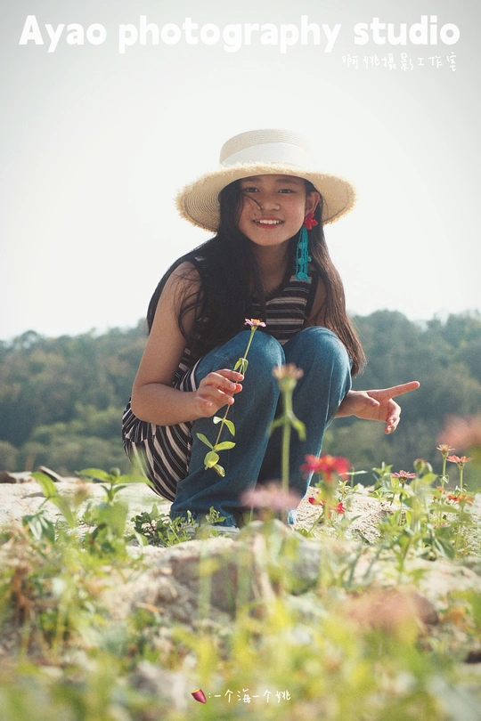 一位戴帽子手持花的年轻女子坐在田野里
