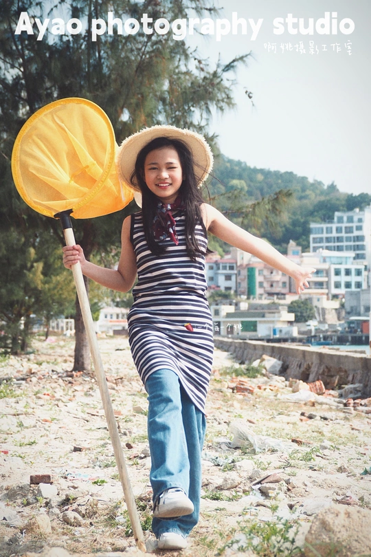 一个小女孩戴着帽子拿着棍子走在沙滩上