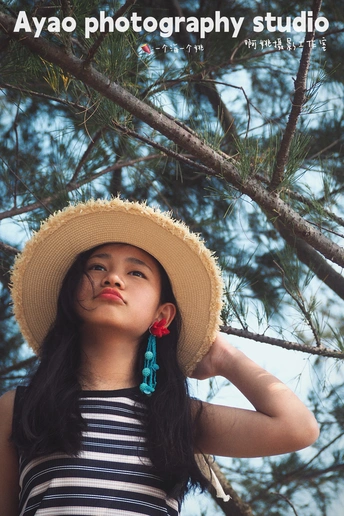 一位年轻女子戴着草编帽子在一棵松树下面