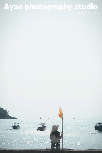 戴帽子的人坐在长凳上 眺望着有船只的海洋 还有一个人在放风筝。