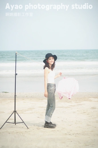 一位戴帽子的年轻女子在沙滩上拿着粉色雨伞