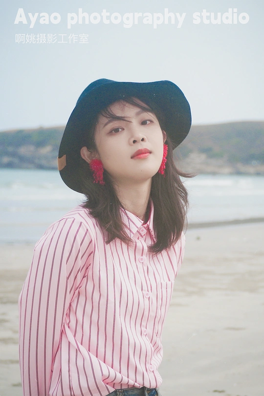 一位穿着条纹衬衫和黑色帽子的年轻女子在海滩上靠近水边摆姿势
