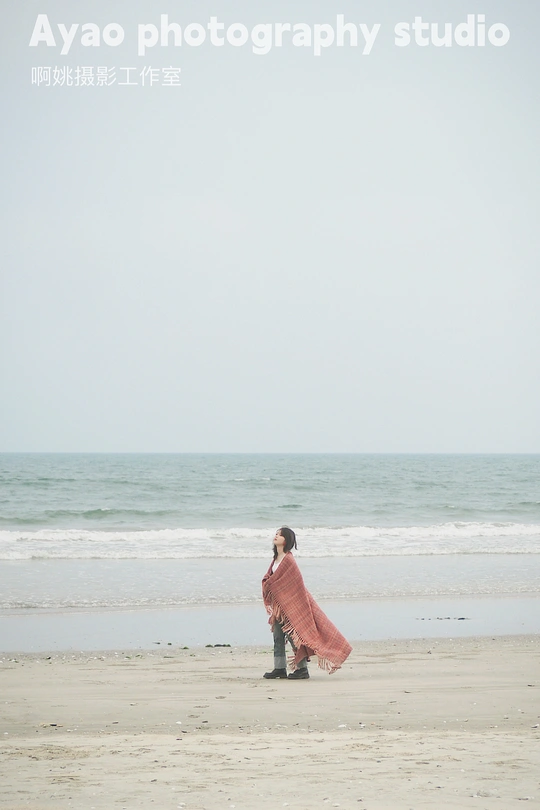 一位穿着红衣服的女人正在靠近海洋的海滩上行走。