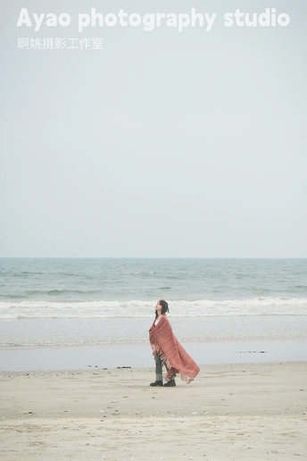 一位穿着红衣服的女人正在靠近海洋的海滩上行走。