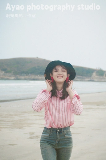 一位穿着条纹衬衫和黑色帽子的年轻女子站在海滩上