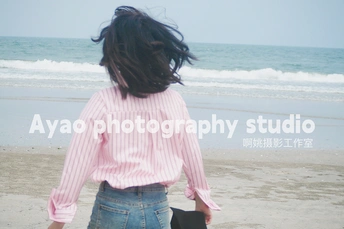 一个穿粉色衬衫的年轻女子在靠近海洋的沙滩上行走 同时拿着一个箱子。