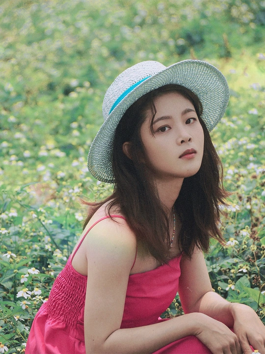 一位穿着红裙子和帽子坐在花田中的美丽年轻女子