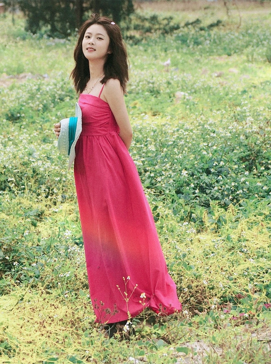 一位穿着红裙子的年轻女子站在草地上花丛中