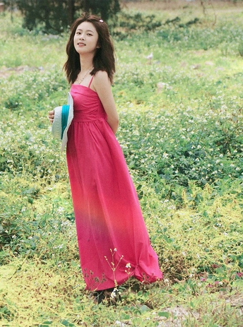 一位穿着红裙子的年轻女子站在草地上花丛中