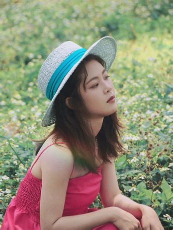 一位穿着蓝色帽子和粉色裙子的年轻女子坐在花丛中