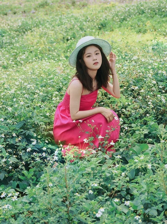 一位穿着红色连衣裙和帽子坐在绿色花丛中的年轻女子