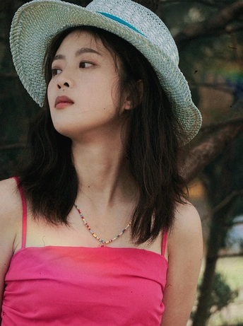 一位穿着蓝色帽子和粉色连衣裙的年轻女子在大型树前摆姿势