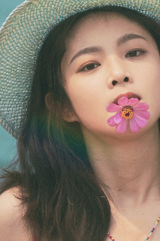 一位戴着草帽的年轻女子嘴里含着粉色花朵