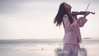 一位穿着粉红色连衣裙的年轻女子在靠近海洋的海滩上演奏小提琴