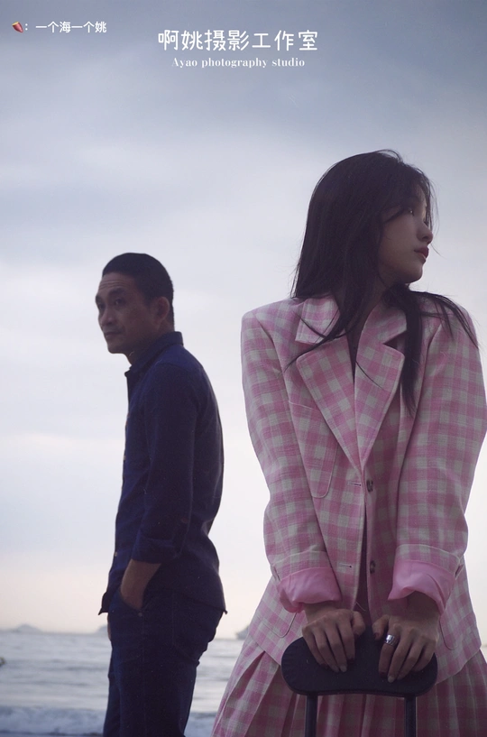 一位穿粉色外套的女人站在一位穿大海报电影的男人旁边