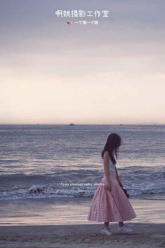 一位穿着粉红色连衣裙的年轻女子在靠近海洋的海滩上行走。