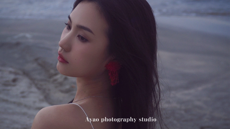 一位穿着红裙子的女士戴着耳环站在海滩附近的水边