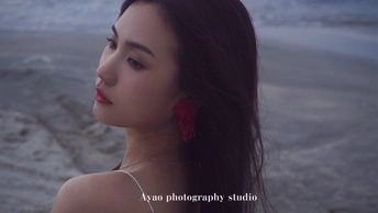 一位穿着红裙子的女士戴着耳环站在海滩附近的水边