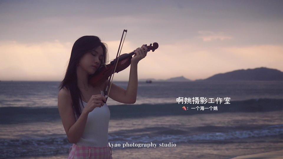 一位穿着连衣裙的年轻女子站在靠近海洋的海滩上 拿着一把小提琴