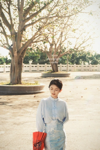 一位穿着蓝色和服的年轻女子 手拿红色手提包 打着红色雨伞在街上走。