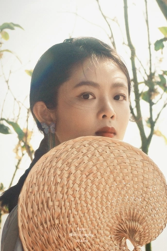 一位年轻女子戴着草编帽子 拿着篮子站在一棵树前。