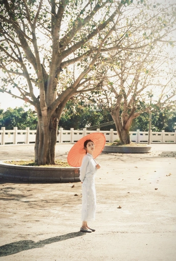 一位穿着全白的年轻女子站在街的中间 一个小女孩拿着红伞。