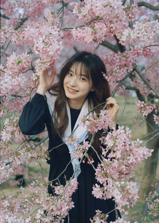 一位年轻女子拿着粉色花朵站在樱花树下